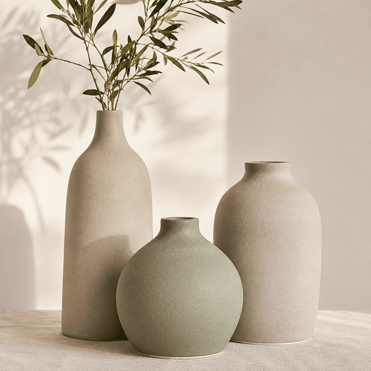 Three matte ceramic vases of different heights in greige and sage, grouped together